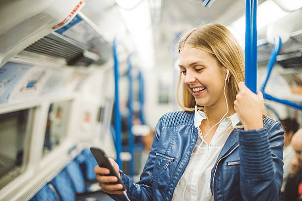 frau in der metro schaut mit kopfhörern im ohr lachend auf ihr handy