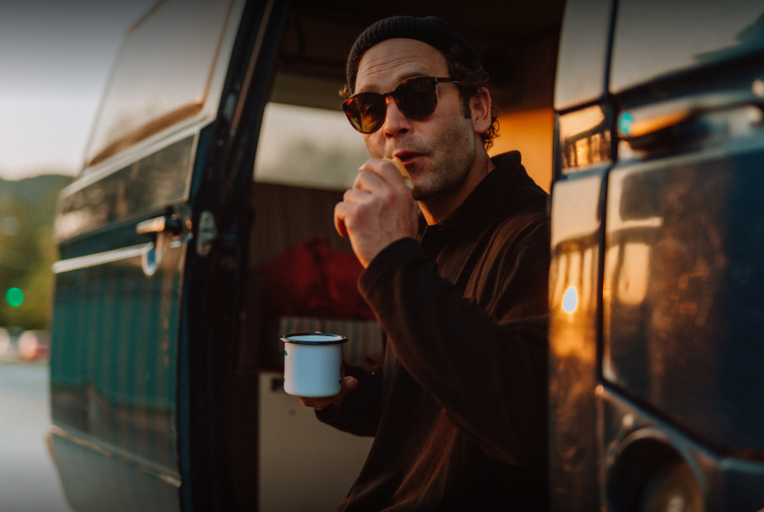 Der Sänger Bosse mit Sonnenbrille und Kaffee in der offenen Tür eines Vans