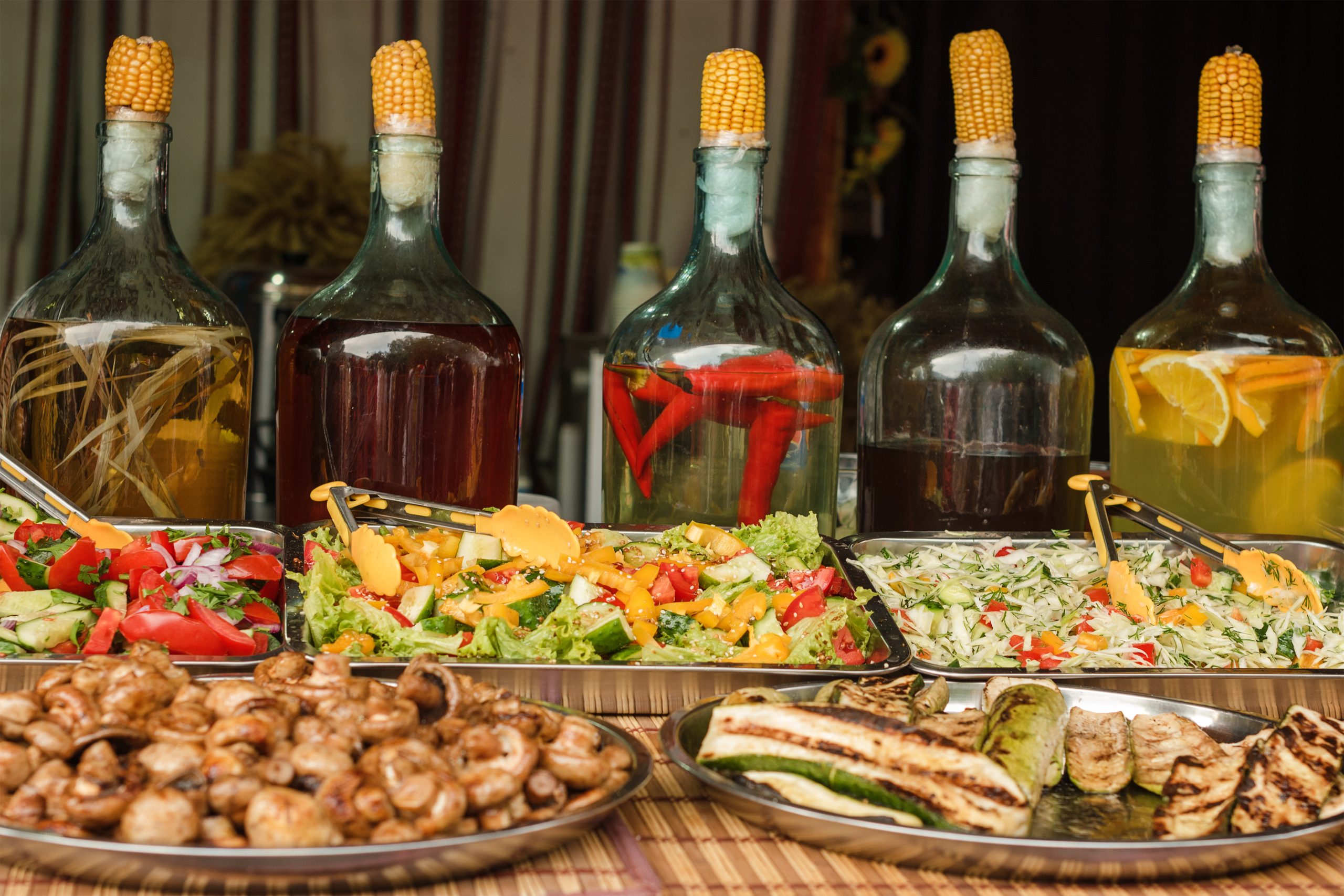 Platten mit Fleisch und Salaten stehen auf einem Tisch. Im Hintergrund sind verschiedene Flaschen zu sehen, die mit einem Maiskolben verschlossen sind. Platten mit Fleisch und Salaten stehen auf einem Tisch als Symbolbild für Gourmet Festivals