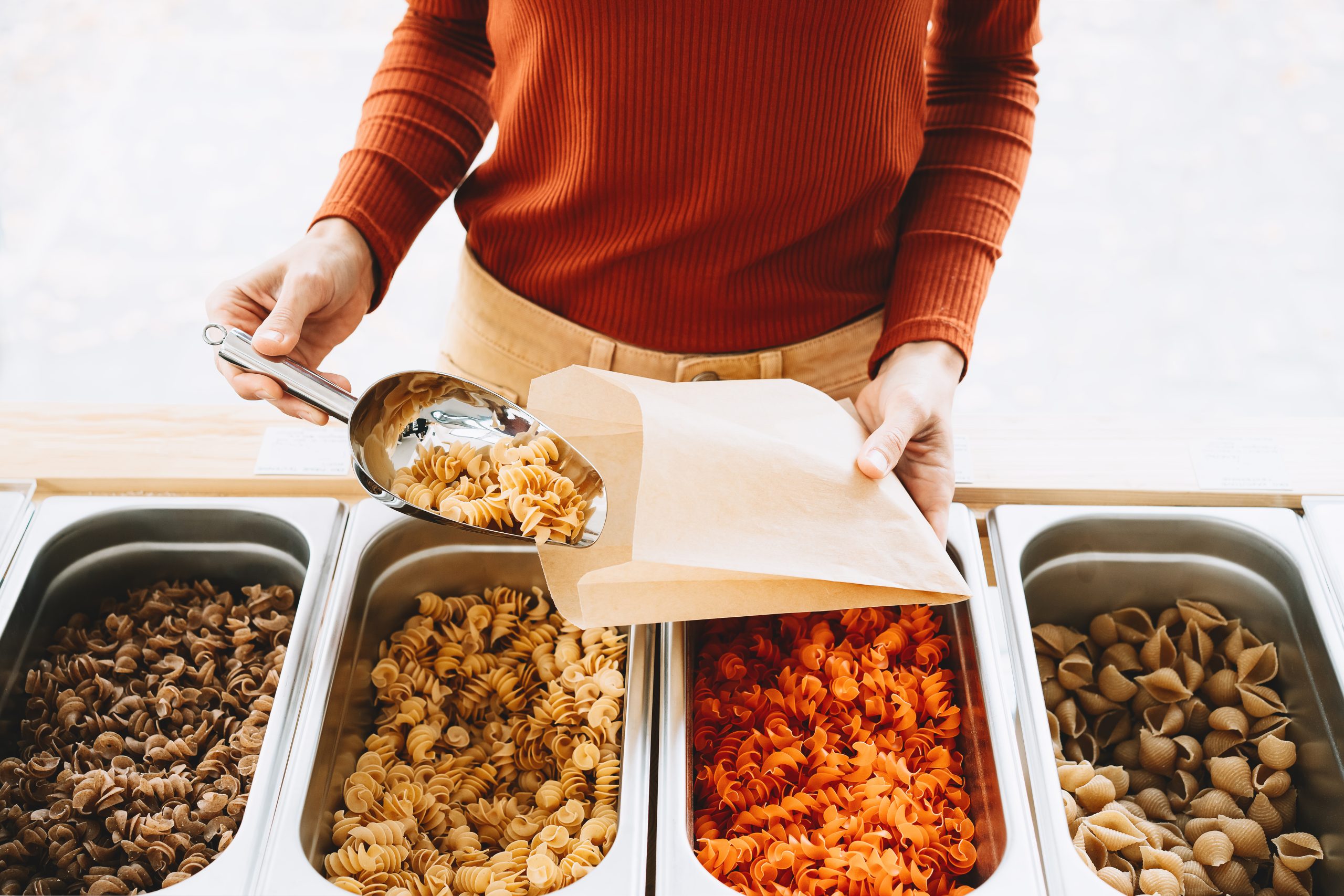 Frau füllt Nudeln mit einer Schaufel in eine Papiertüte.