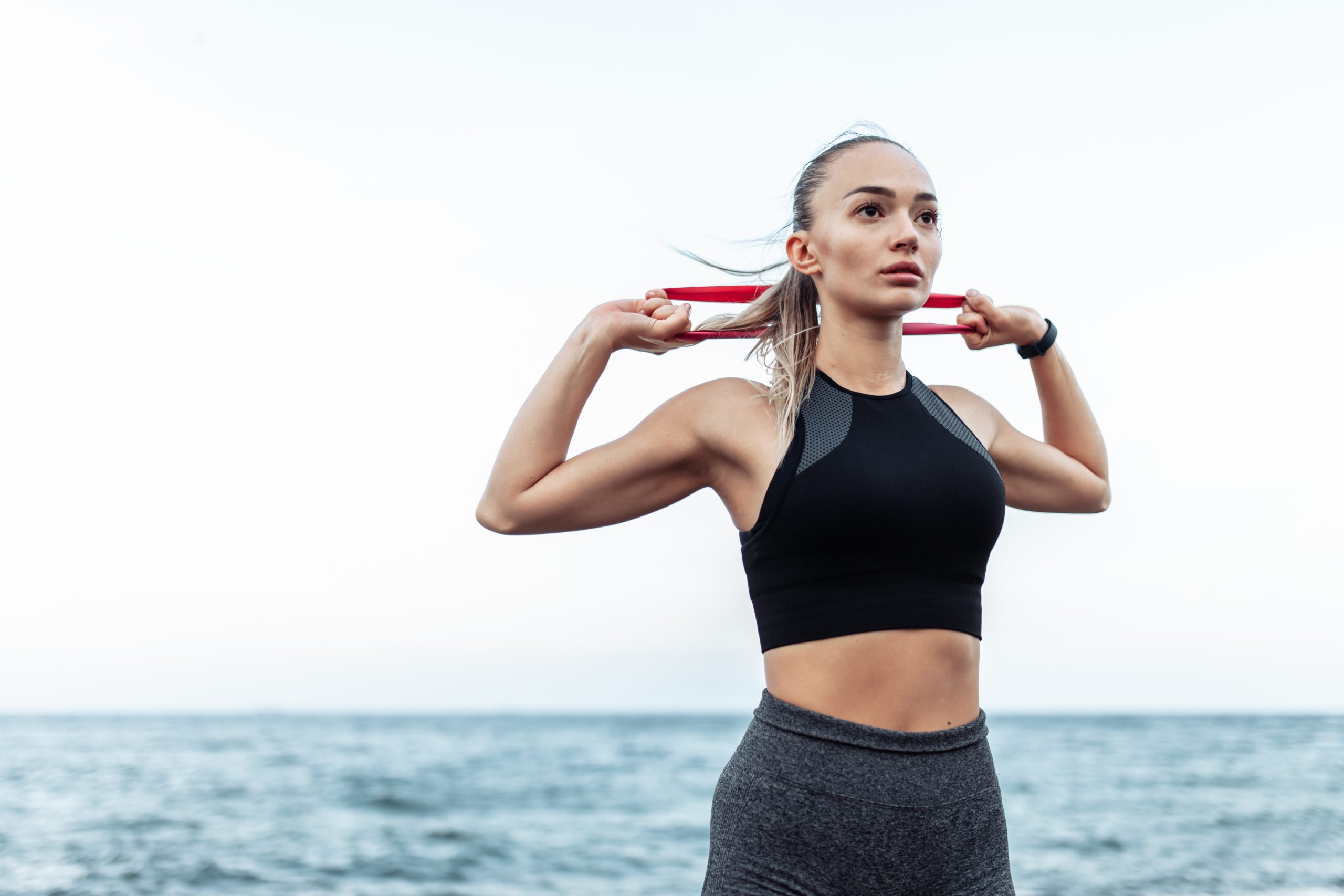 Eine junge Frau trainiert am Strand mit einem elastischen Fitness-Band.