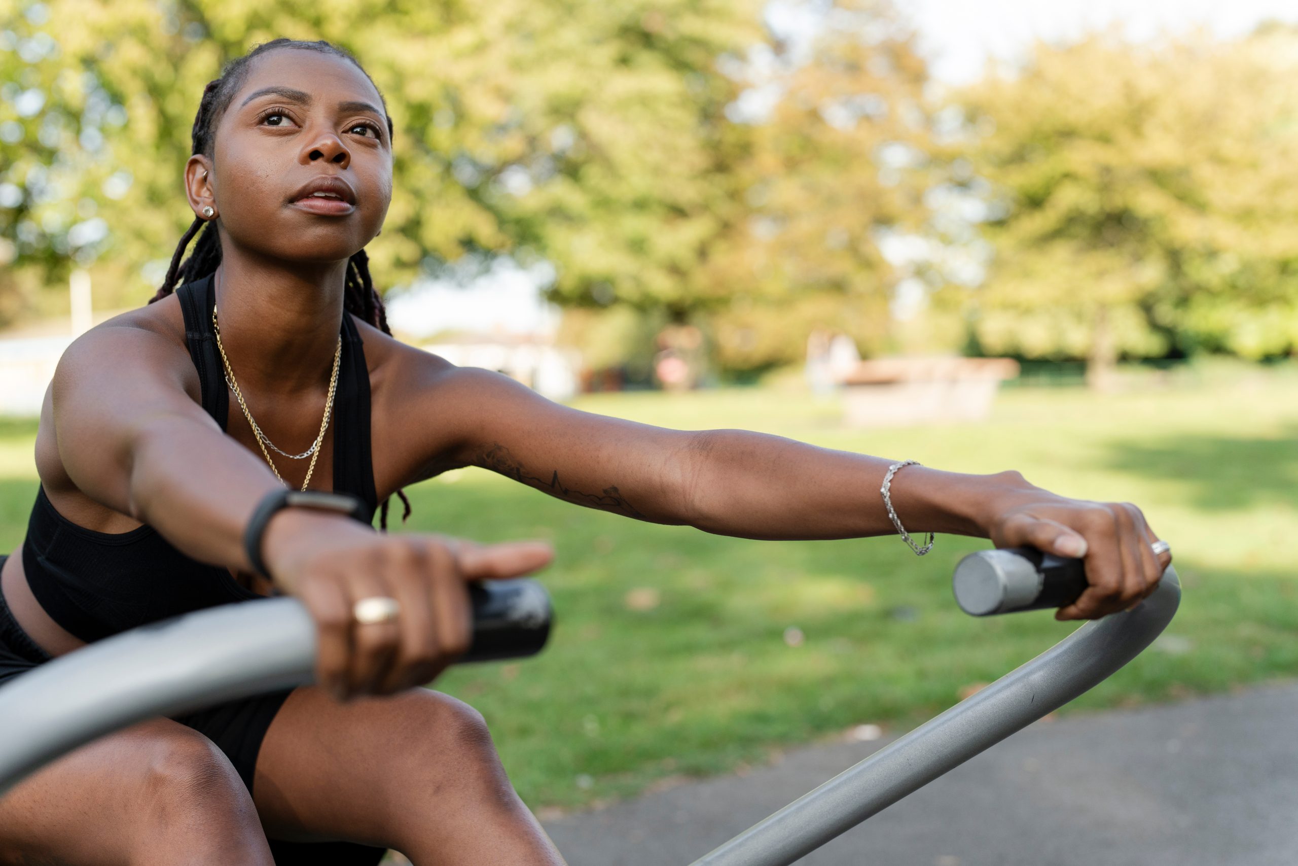 Eine junge Frau trainiert draußen an einem Rudergerät.