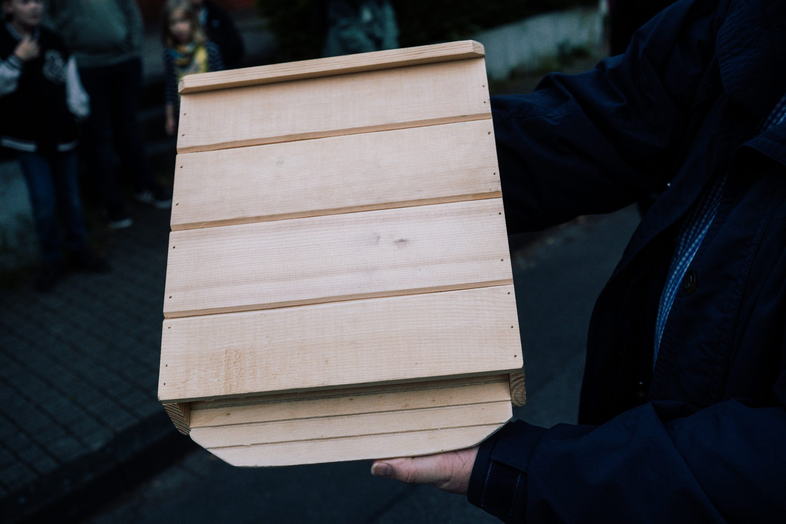 Eine Person hält einen Fledermauskasten aus Holz in der Hand