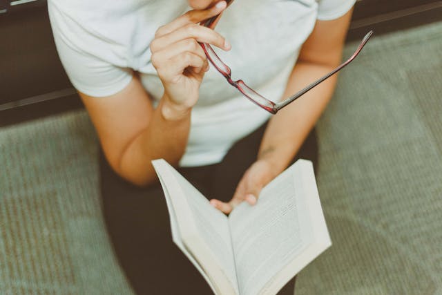 ein Mann liest ein Buch und hält dabei seine Brille in der Hand